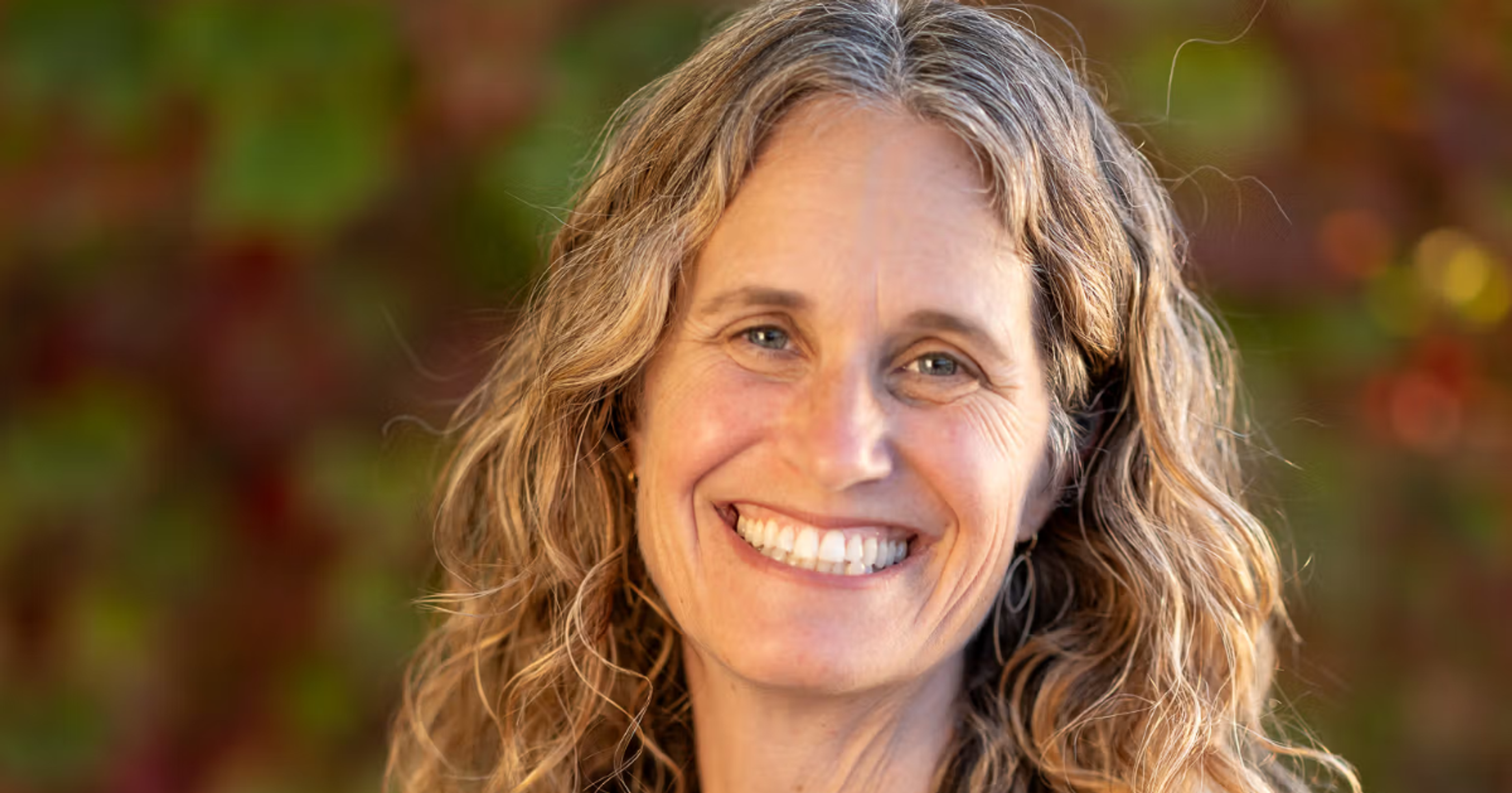 Robin Kaplan smiling outdoors in a navy blouse, with shoulder-length hair and a softly blurred background