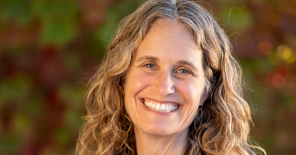 Robin Kaplan smiling outdoors in a navy blouse, with shoulder-length hair and a softly blurred background