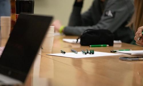 Et møtebord fylt av penner, papir, kaffe og en pc