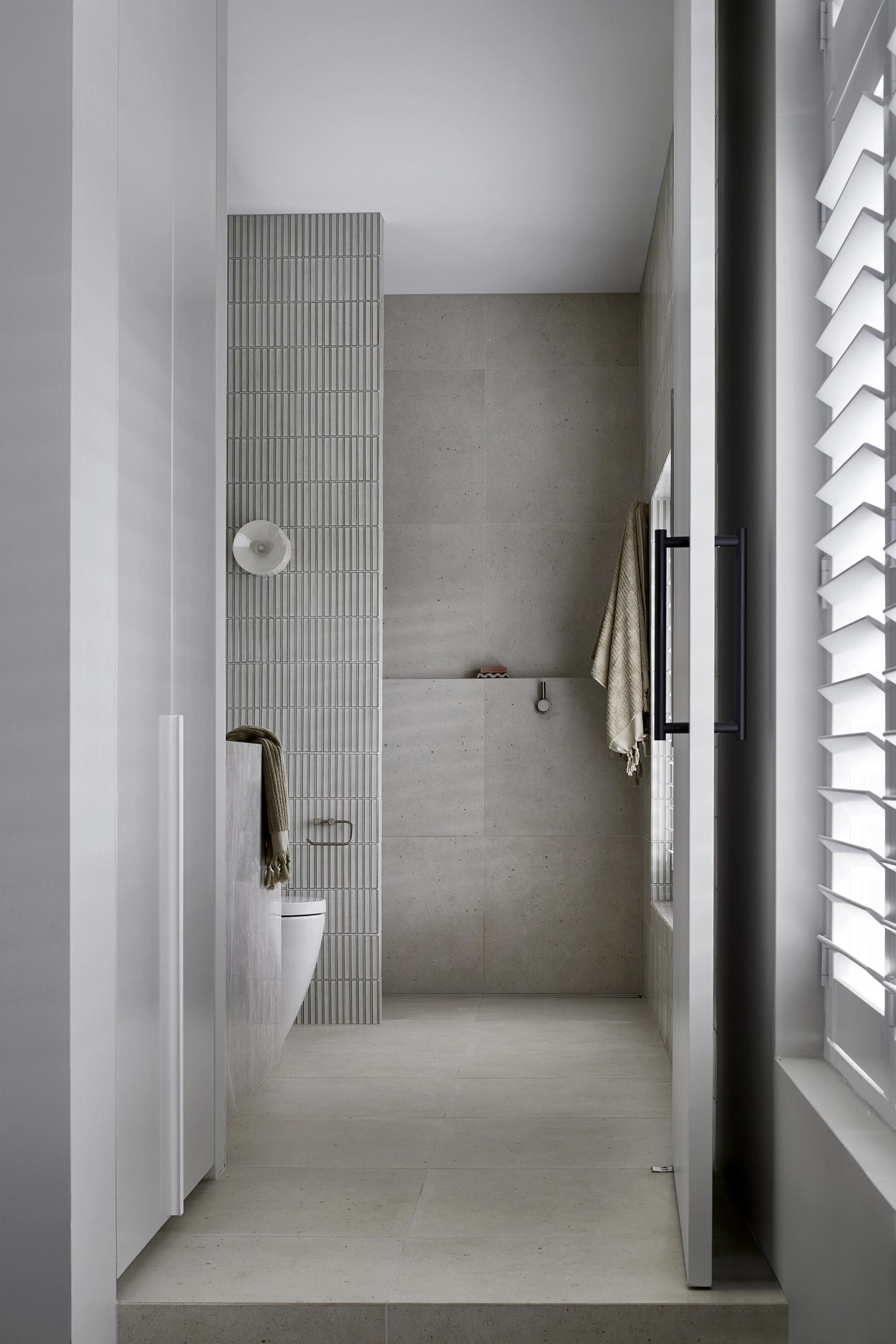 Main bathroom in the South Yarra Townhouse featuring a walk-in shower, textured feature tiles, large-format stone tiles and a minimalist palette.
