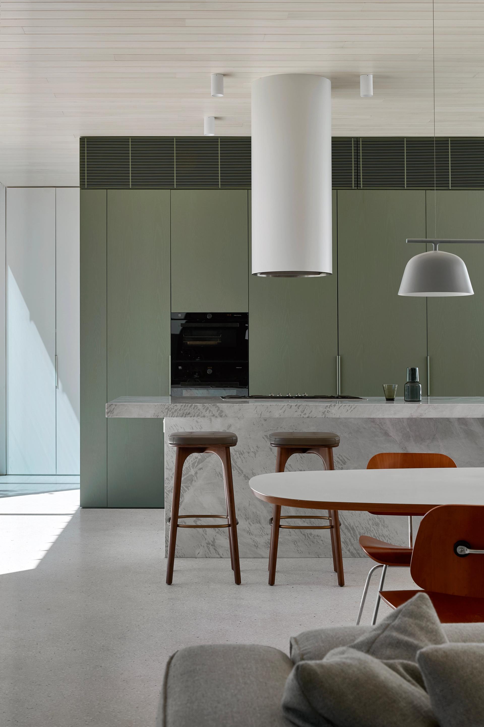Stone island with olive green tall joinery unit concealing butlers pantry behind