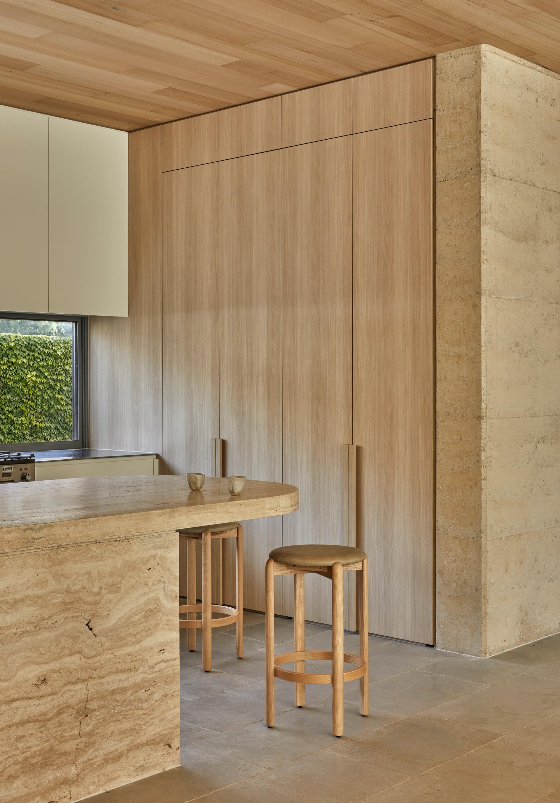 Full-height timber cabinetry and a curved travertine island create a natural gathering point
