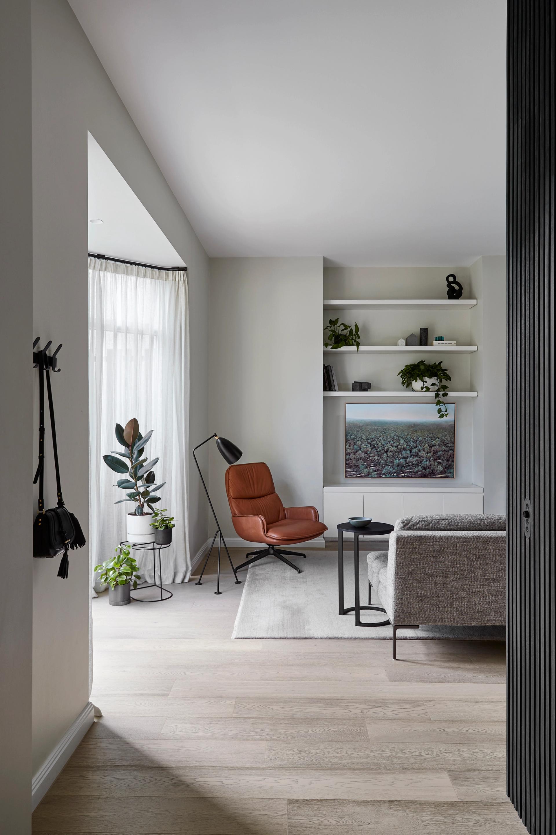 Living room in South Yarra Townhouse with built-in shelving, leather lounge chair and large sheer-curtained window.