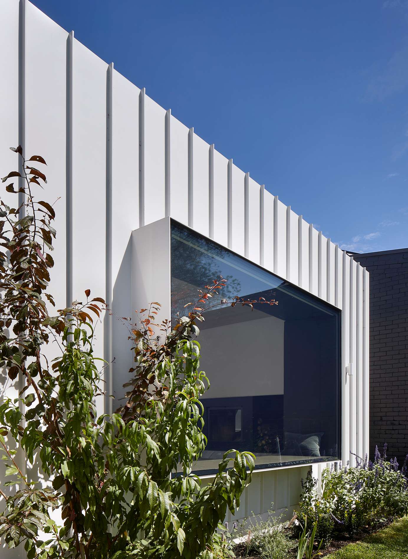 A steel box framed window seat puncuates the white metal clad facade
