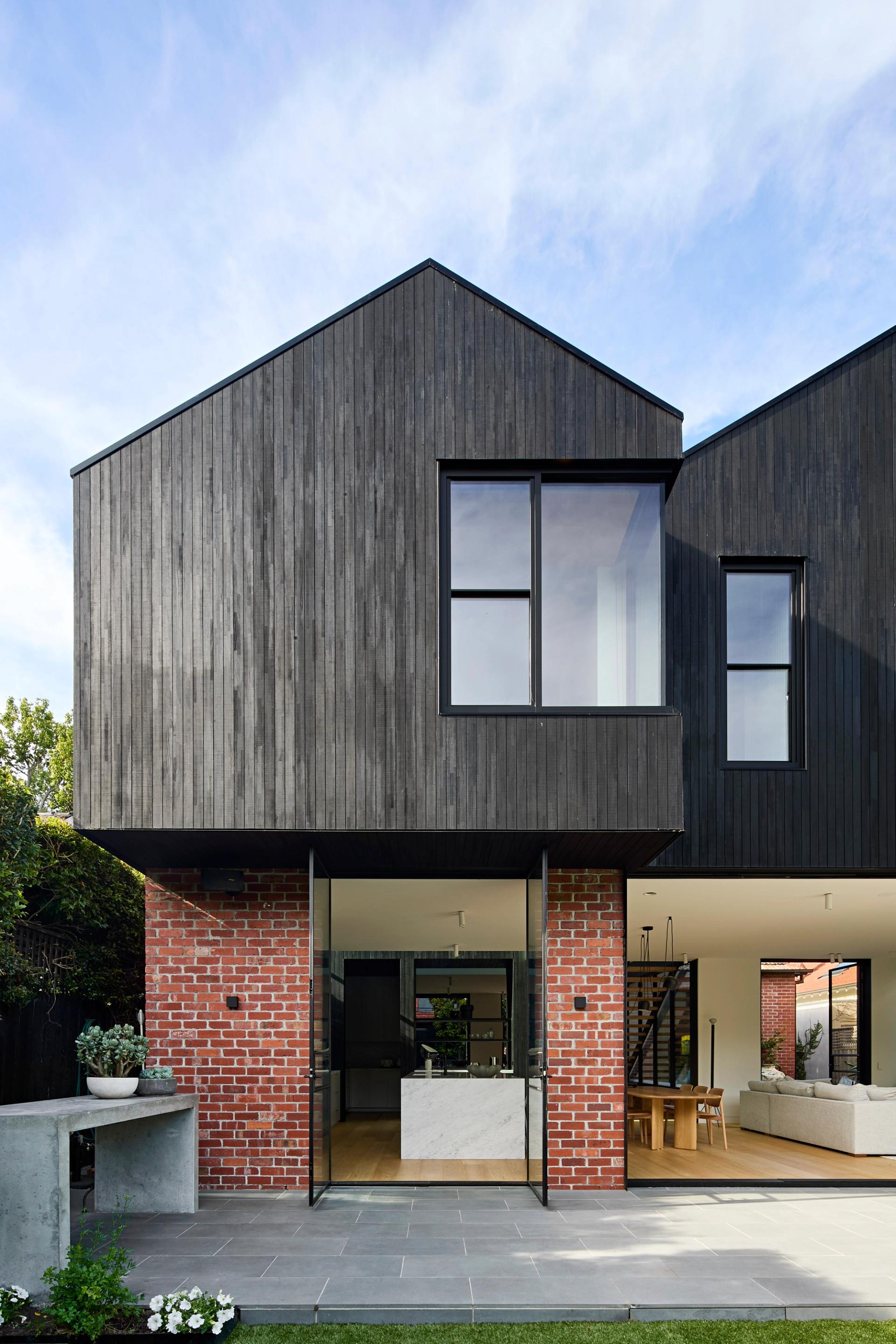 The home's upper volumes feature black stained thermally modified timber cladding, creating clean angular shapes that echo the original roof pitch.