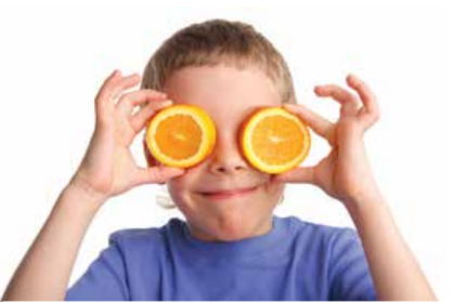 Young child holding orange slices over their eyes.