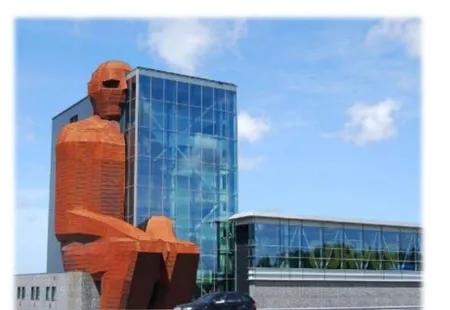 Fotografia budynku Corpus Museum w Holandii — czerwonobrązowa figura siedzącego giganta połączona z częścią budynku o szklanej elewacji.