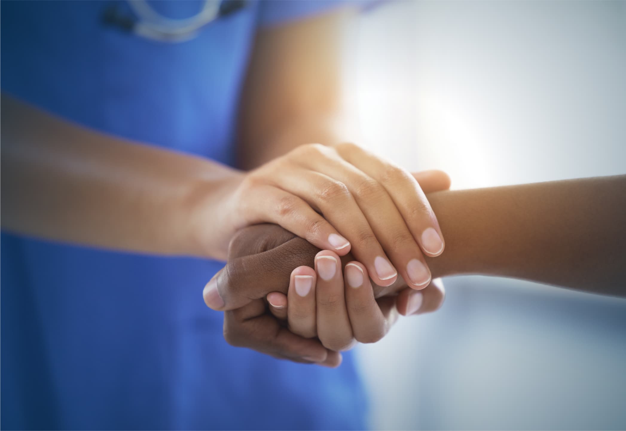 A healthcare provider's hands clasped empathetically around the outstretched hand of her patient.