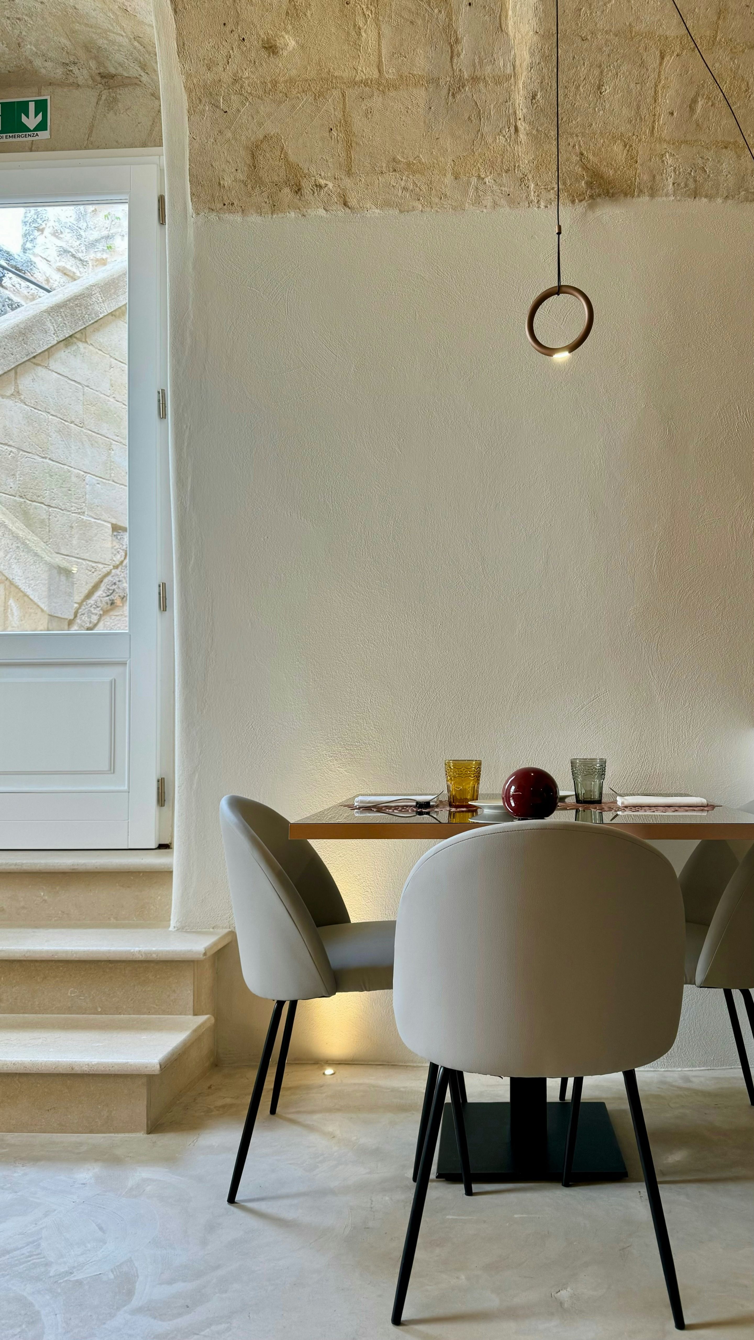 Dining area with a natural stone wall, dining table and a view outdoors in an Italian residence.