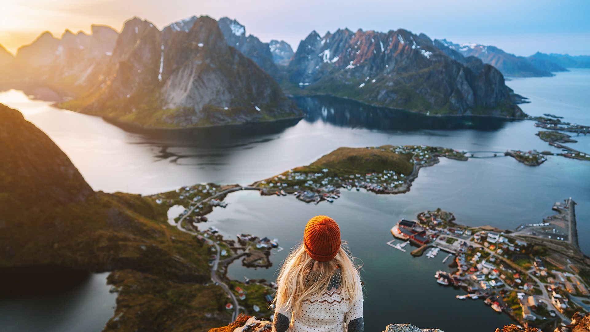Frau mit blonden Haaren und roter Mütze schaut auf die Lofoten.
