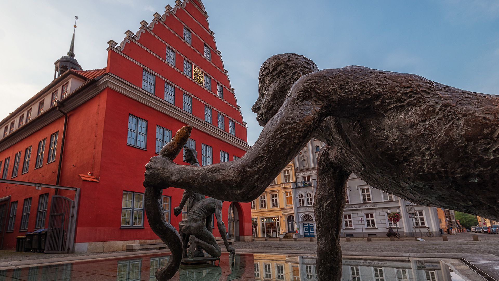 Fischerbrunnen in Greifswald mit Rathaus im Hintergrund.