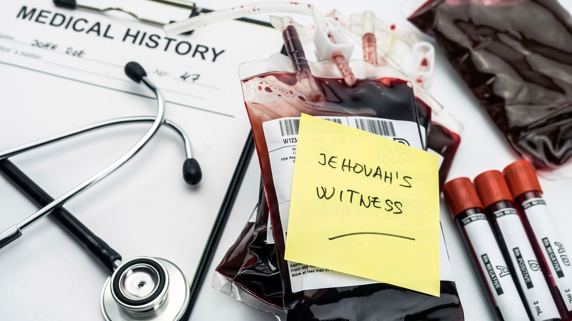 Zettel mit Aufschrift "Zeuge Jehovas" auf Blutkonserve. Daneben Stethoskop und Blutröhrchen.