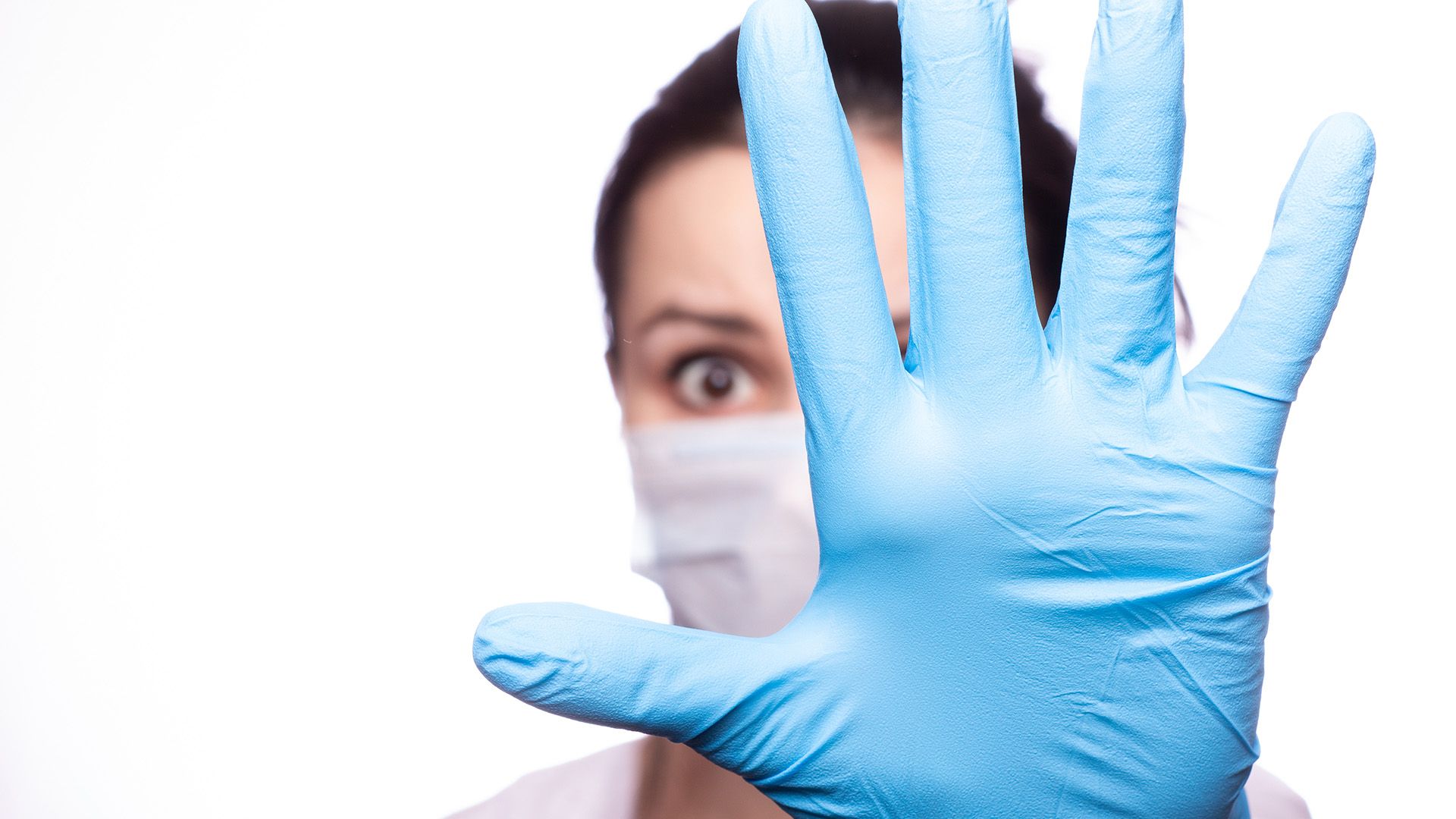 Frau mit Mundschutz und hält Hand mit blauem Handschuh hoch.