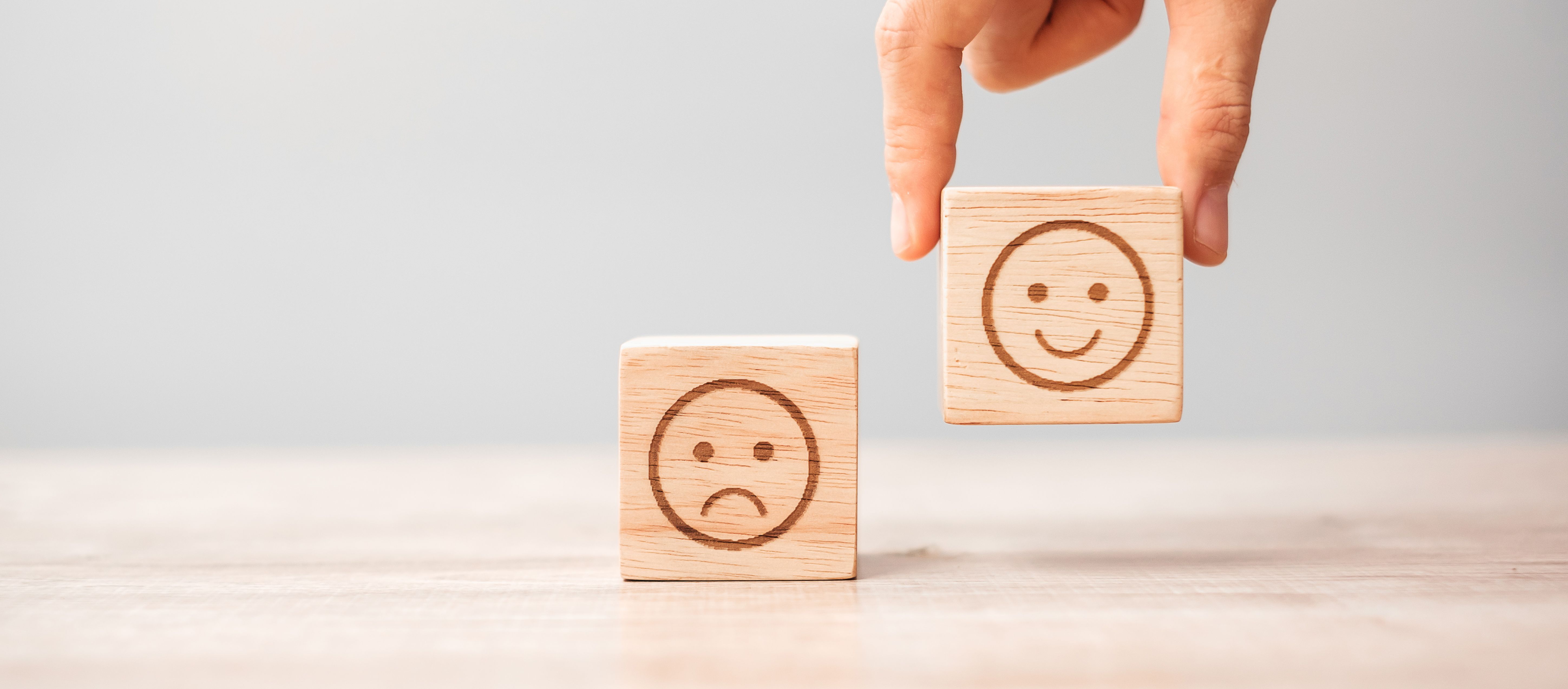 Hand hebt unhappy Smiley Würfel. Daneben auf dem Tisch happy Smile Würfel.