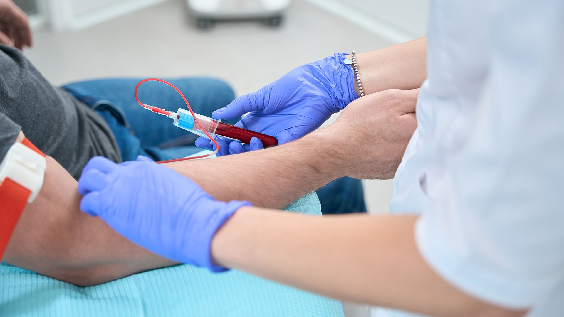 Blutabnahme am Arm mit Stauschlauch, Kanüle und Röhrchen.