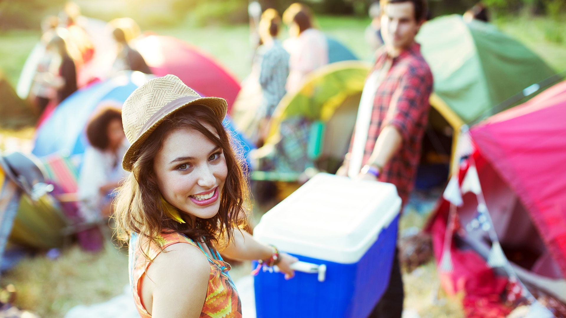 Frau und Mann tragen blaue Kühlbox über den Festival Zeltplatz.