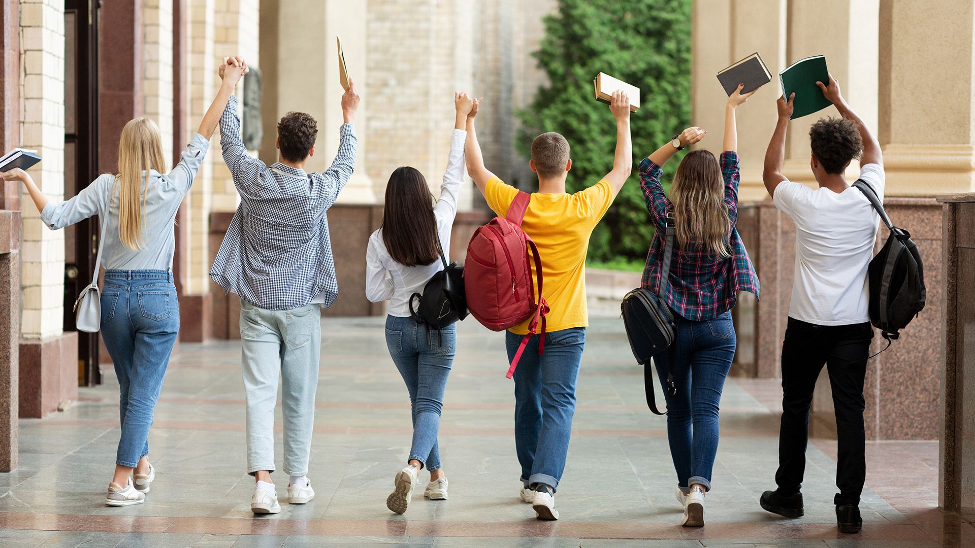 Studierende in der Rückansicht laufen über den Campus mit hochgehaltenen Händen. 