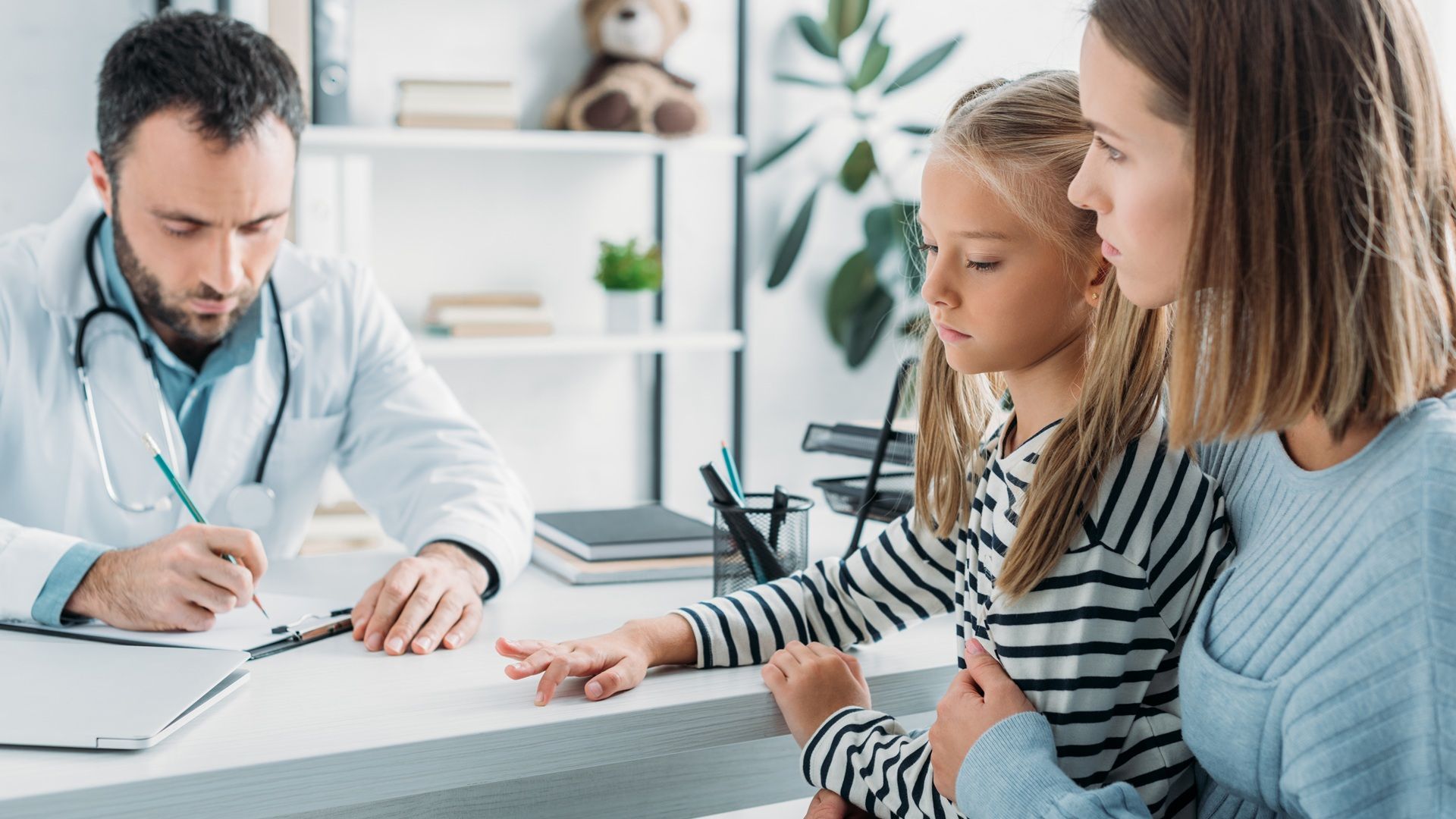 Mutter mit Kind auf dem Schoß beim Arzt im Behandlungszimmer.