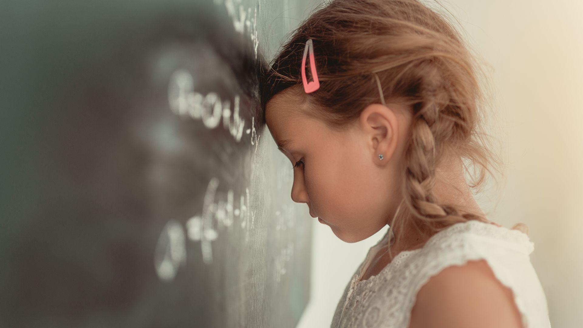 Mädchen lehnt Kopf frustriert gegen Schultafel.