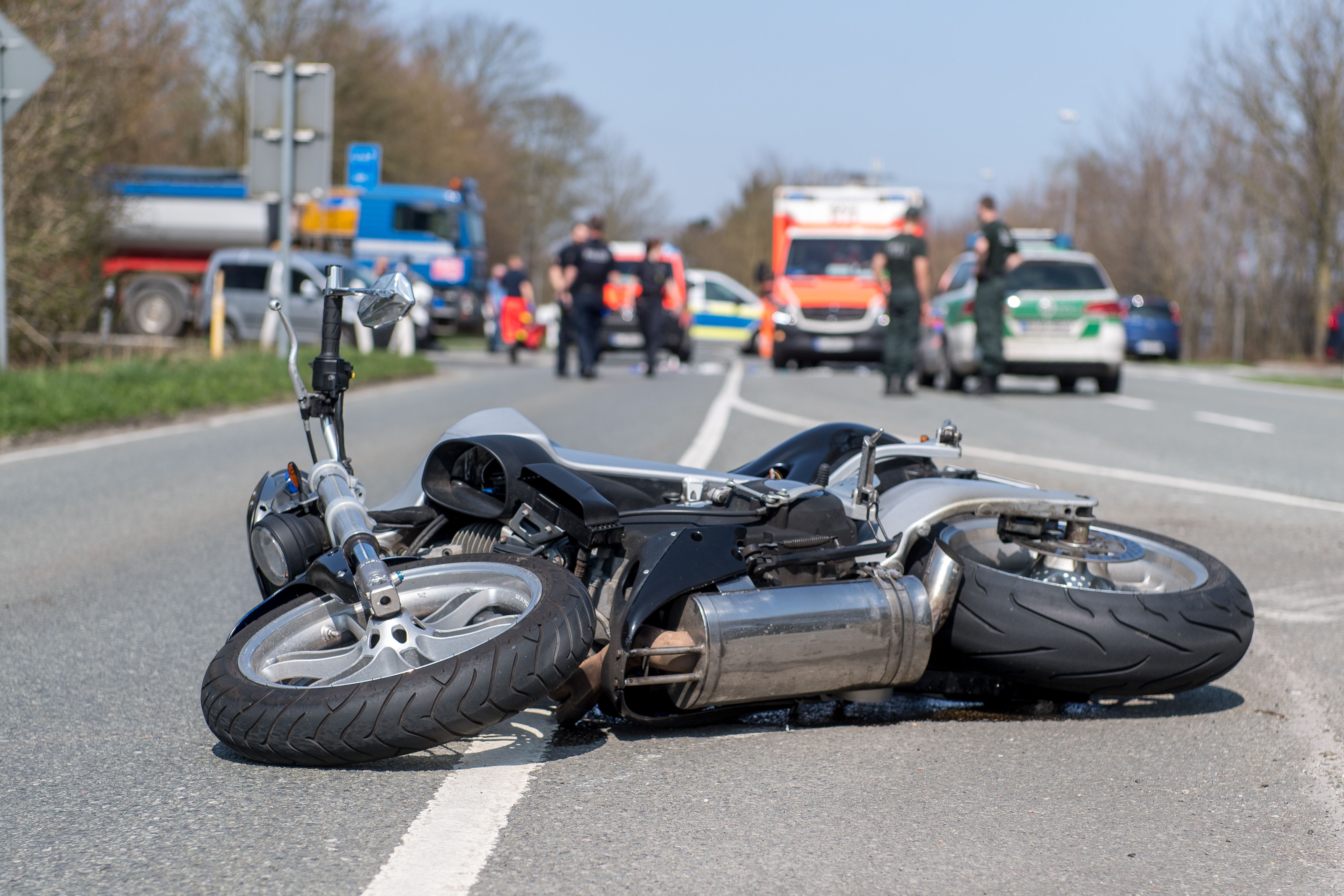 Motorrad liegt nach Unfall auf der Straße, im Hintergrund LKW, Polizei, Krankenwagen und Menschen.