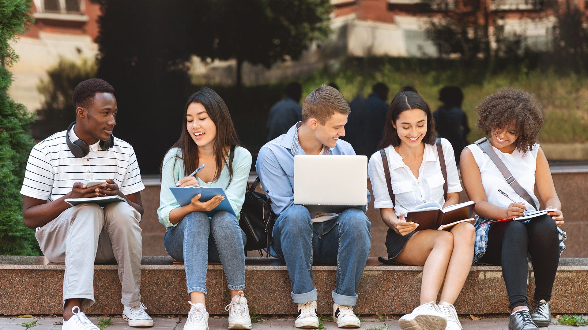 Studierende mit Laptops und Büchern sitzen auf einer Treppe.
