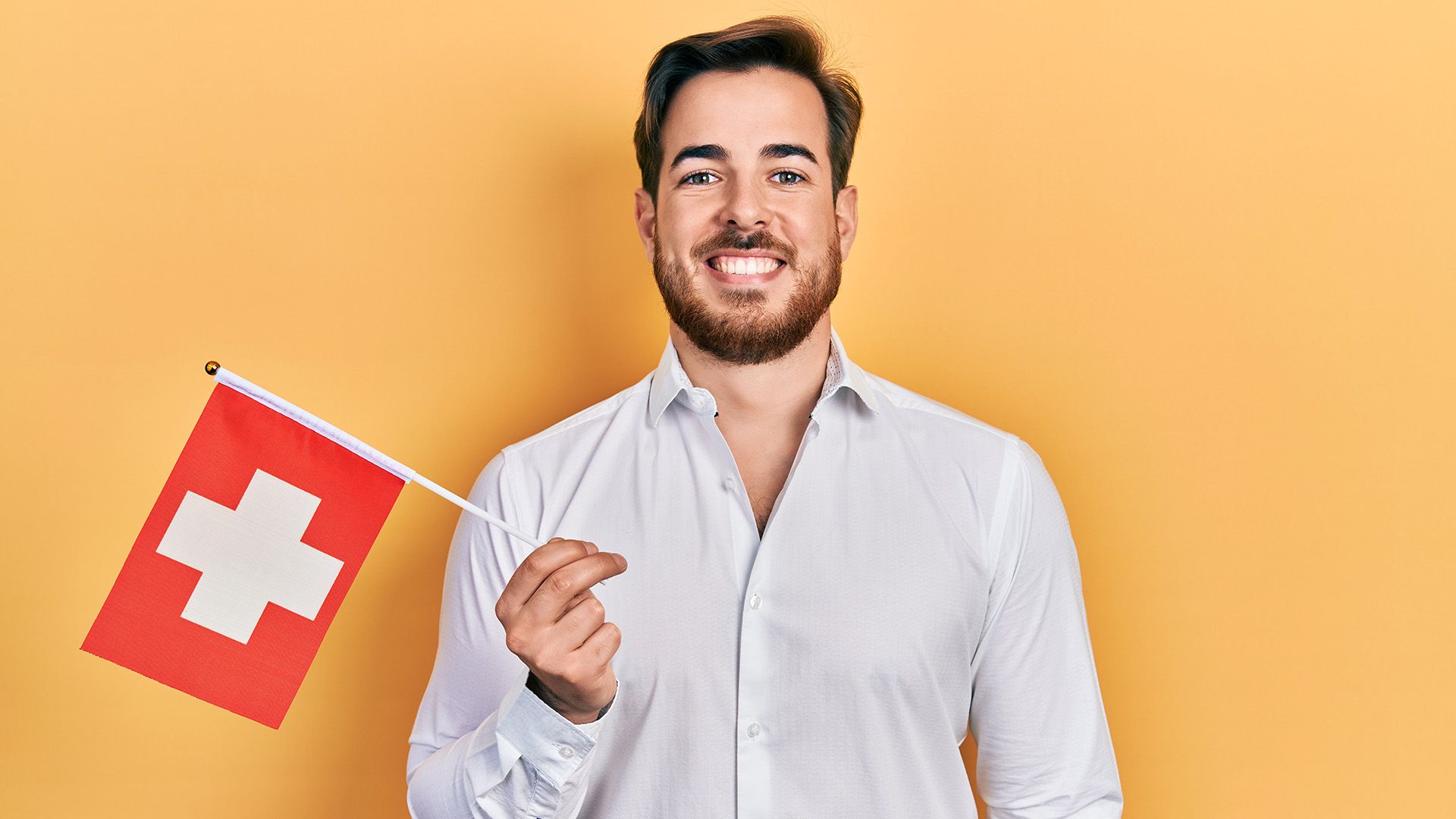 Lachender Mann im weißen Hemd hält Schweizer Flagge in der Hand.