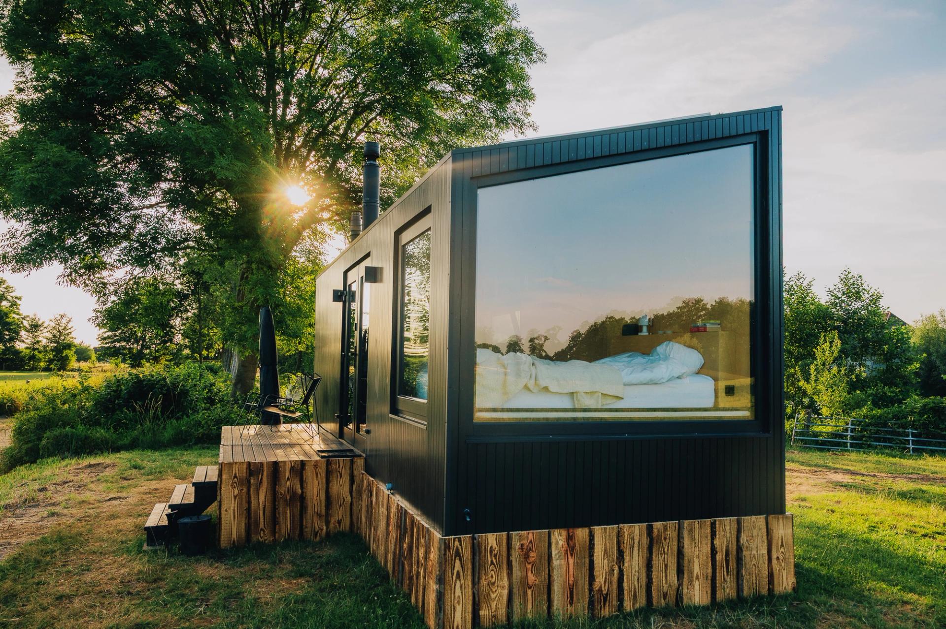 Außenansicht eines Tiny Houses von Raus mit Blick in das große Panoramafenster bei Sonnenschein in Deutschland