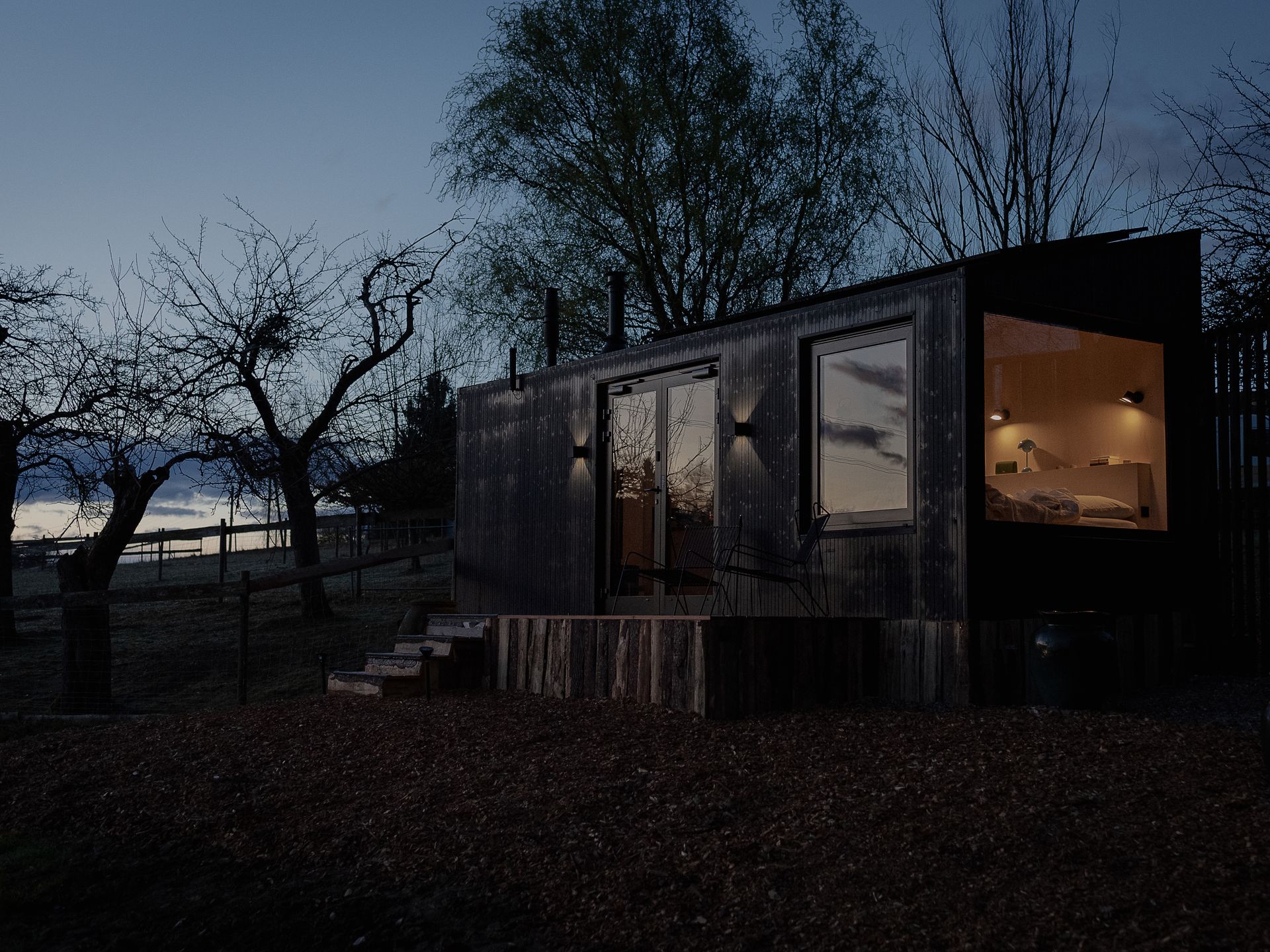 Nachtansicht der Cabin von außen, in der die Lampen neben dem Bett an sind, sodass innen ein warmes Licht herrscht