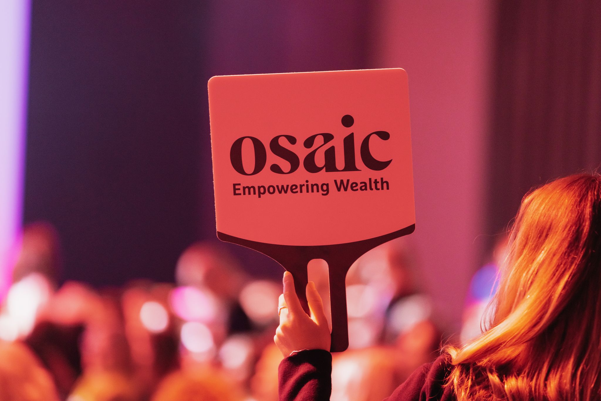 A Financial Professional holds up a sign reading, Osaic Empowering Wealth
