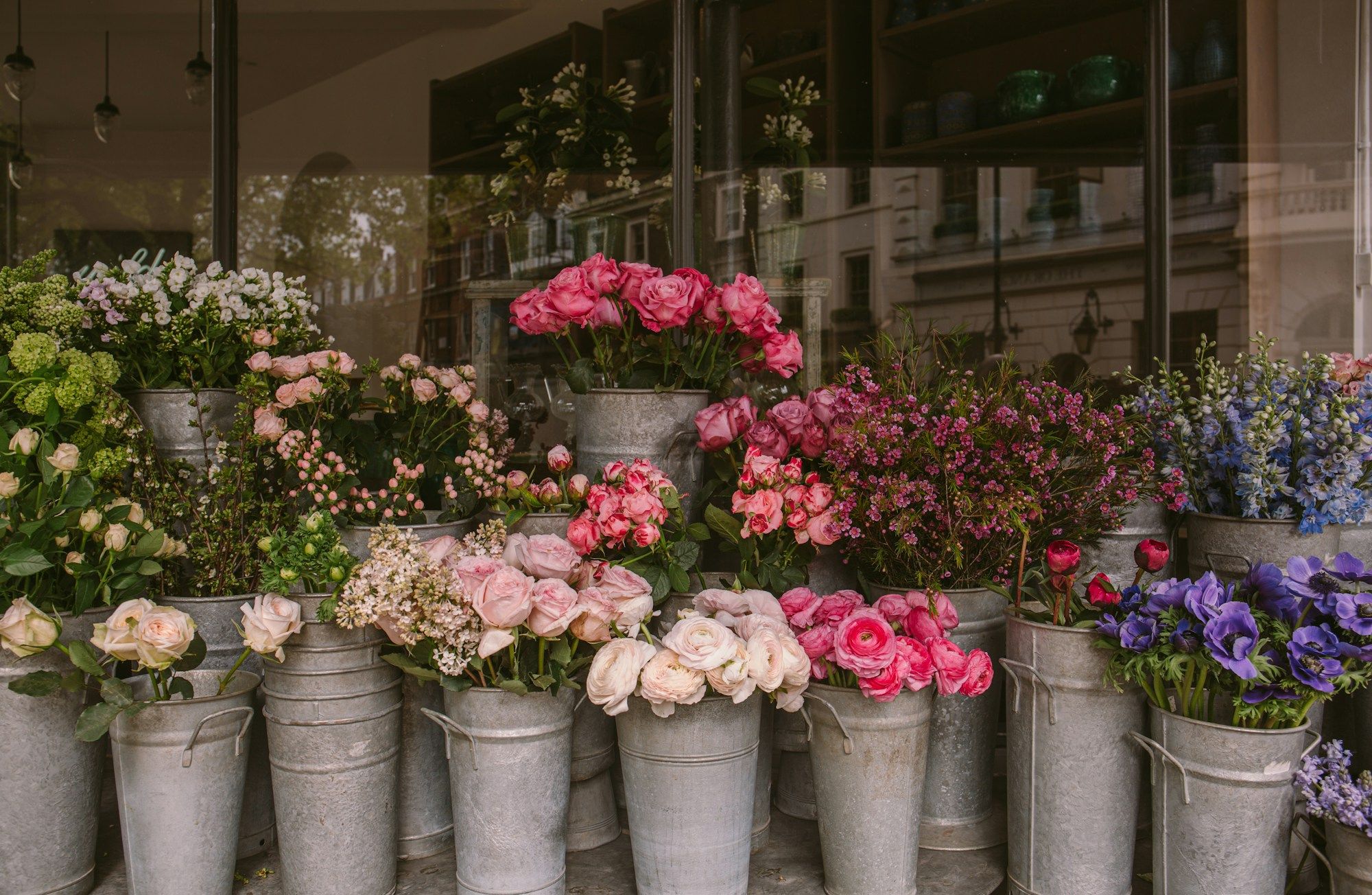Fiori nei secchi di zinco davanti alla vetrina di una bottega