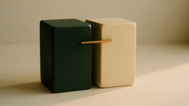 Two painted wooden blocks, dark green and warm cream, connected by a thin brass rod