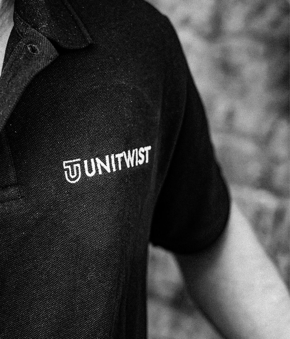 Black-and-white close-up of a person wearing a black Unitwist branded polo shirt, with the embroidered logo in focus.