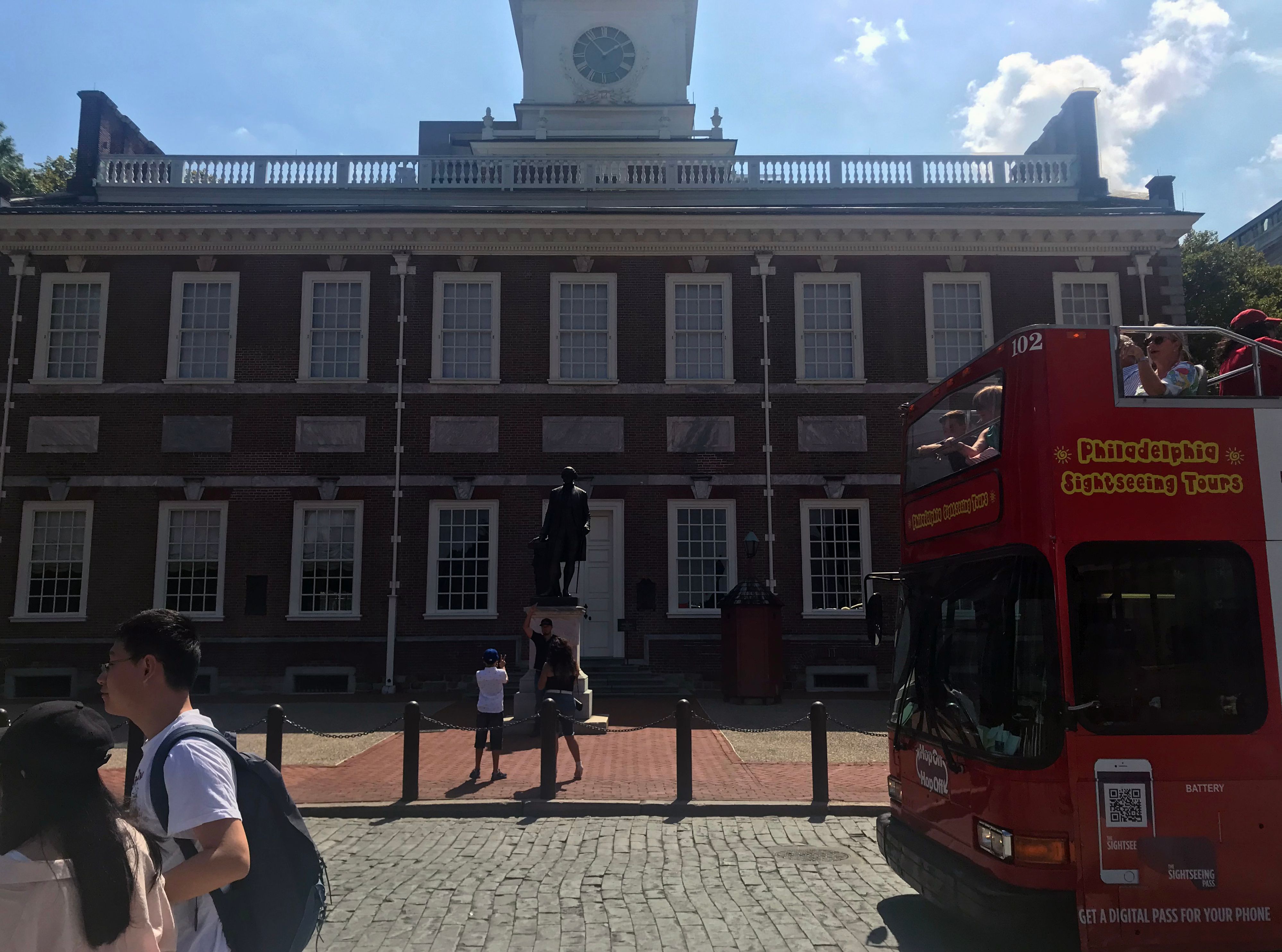 Visitors gathered before the red-brick Georgian facade and white steeple of Independence Hall in Philadelphia.