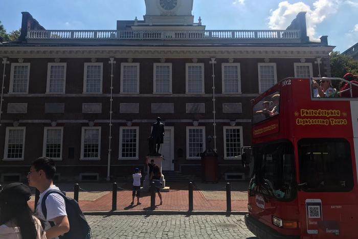 Visitors gathered before the red-brick Georgian facade and white steeple of Independence Hall in Philadelphia.