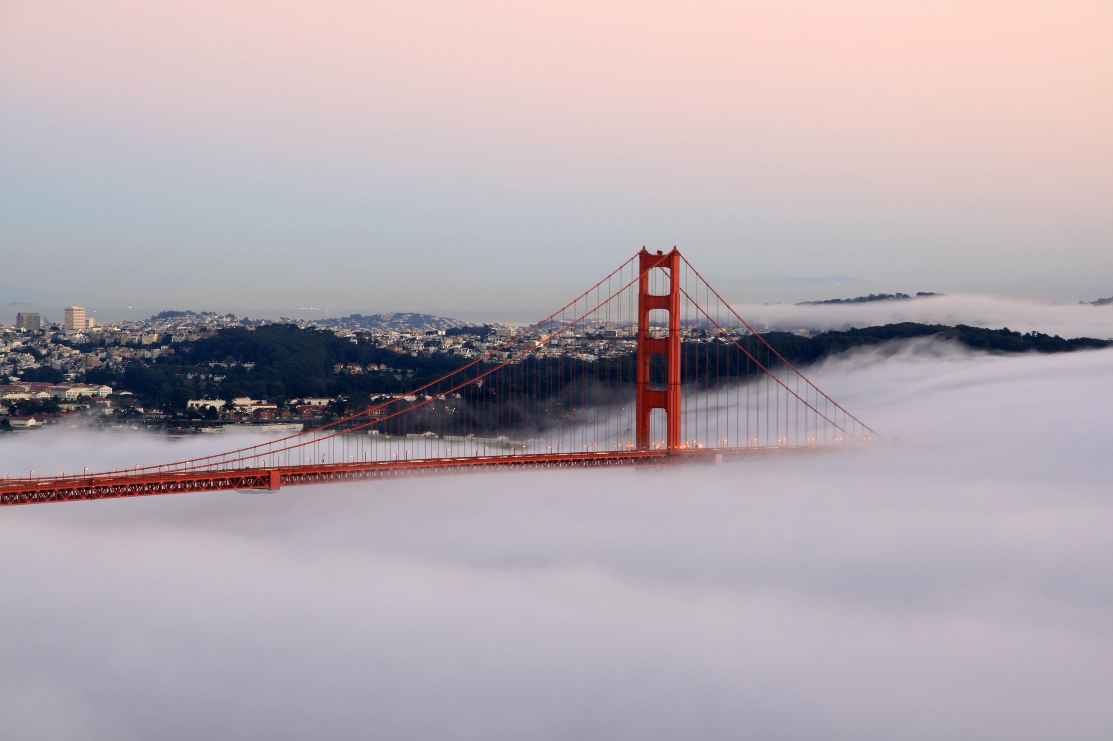 The Golden Gate Bridge at sunset, partly veiled in fog.