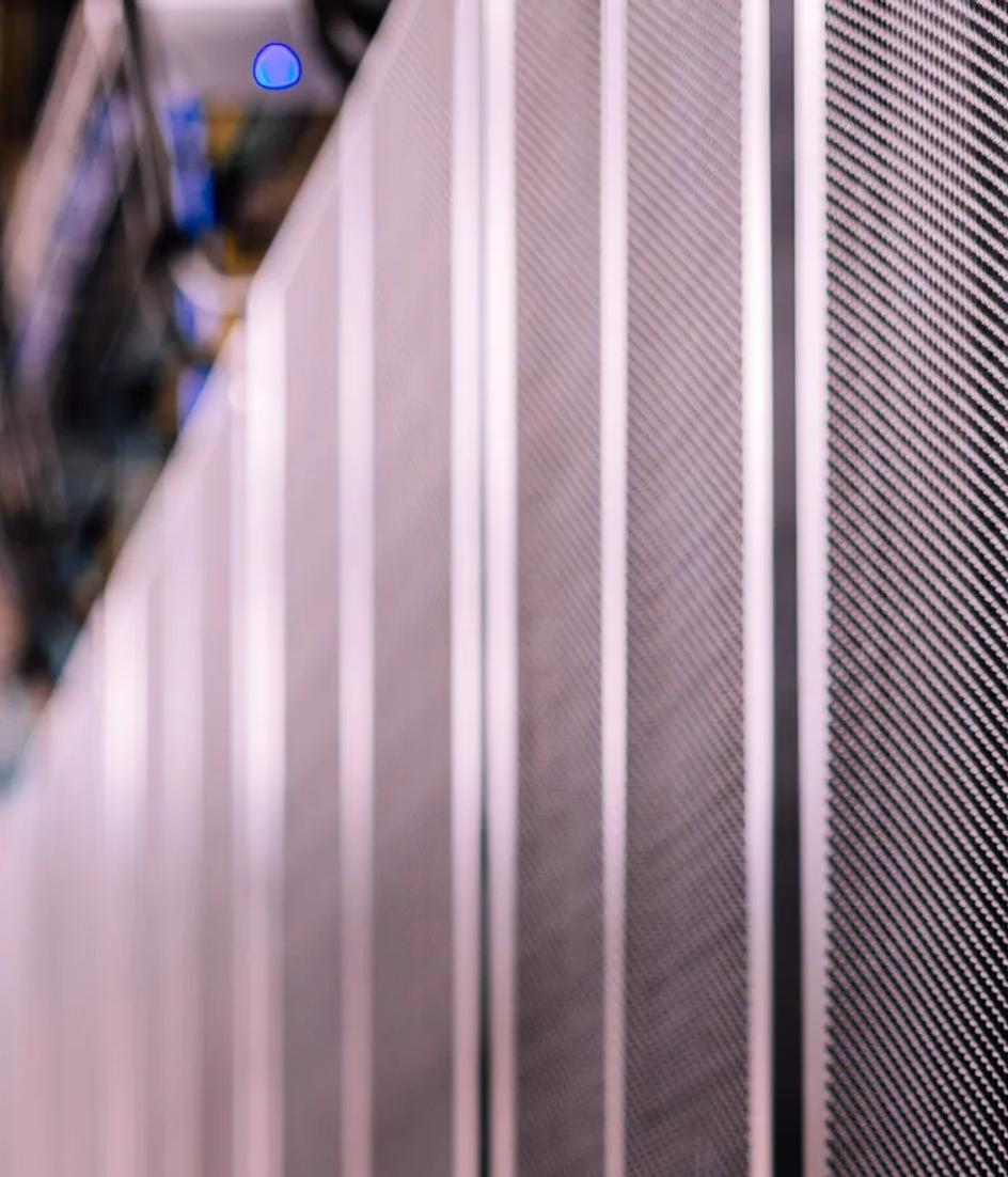 Rows of black server racks in a data centre, with fibre cabling running between the cabinets.