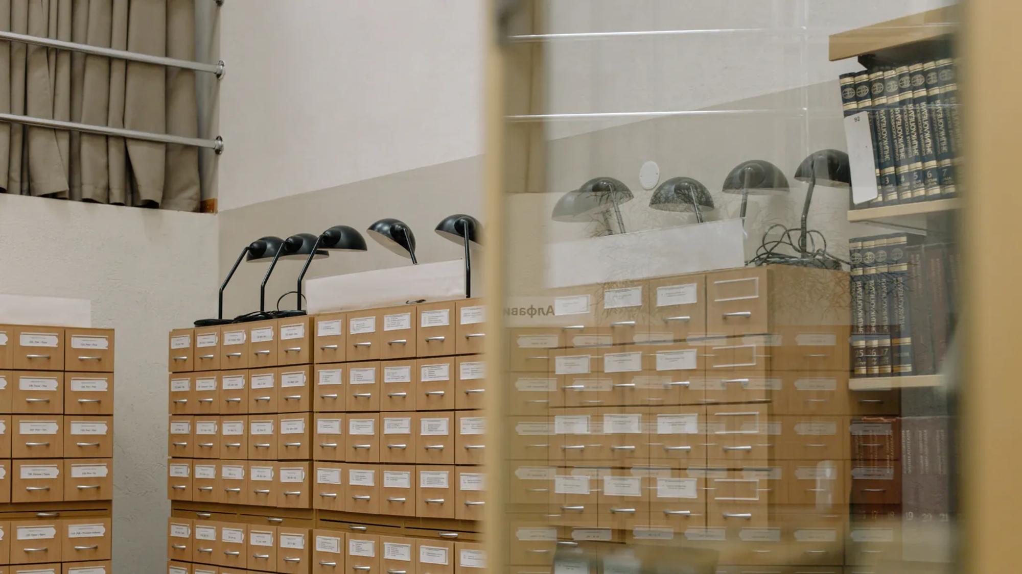 A wooden library card catalogue with rows of labelled drawers and two reading lamps above it.