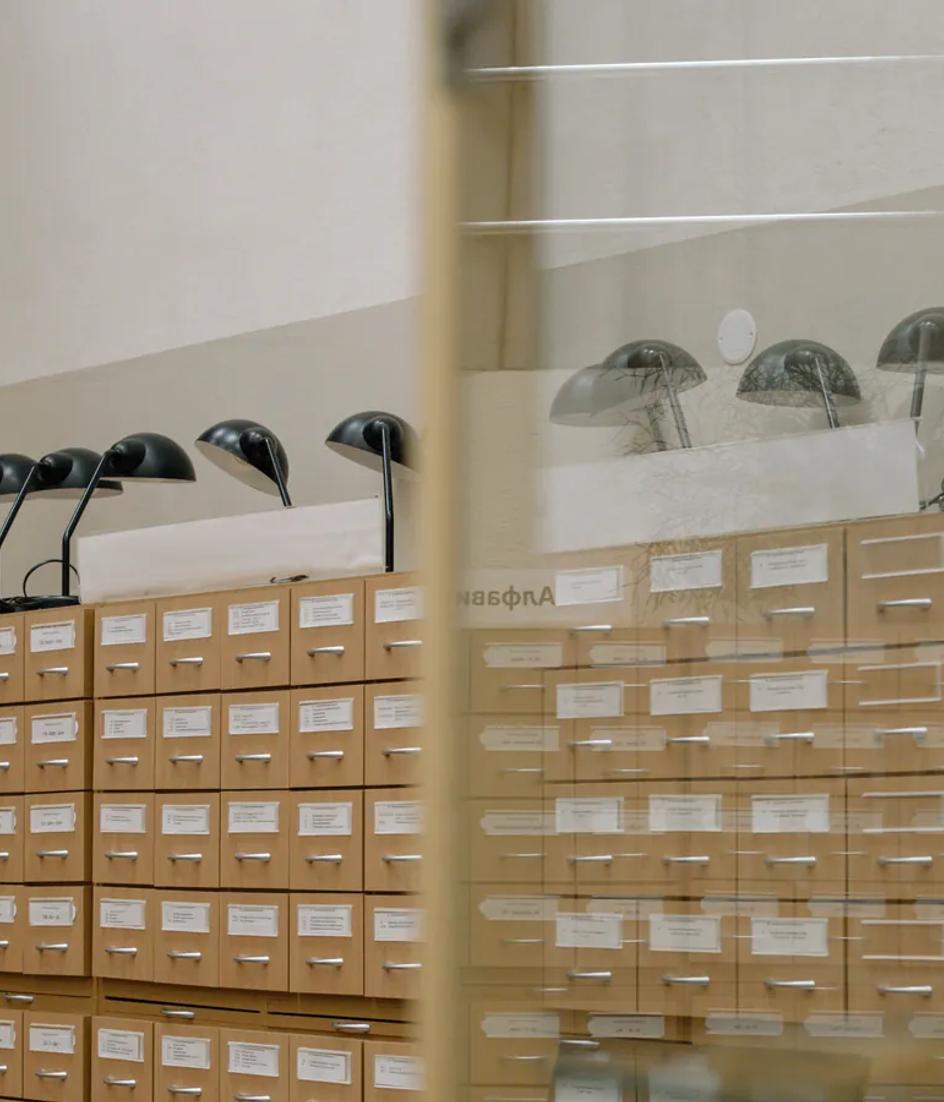 A wooden library card catalogue with rows of labelled drawers and two reading lamps above it.