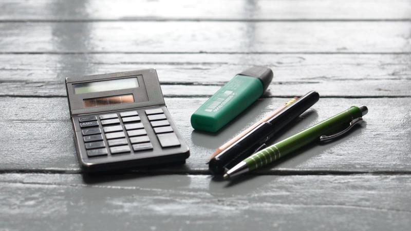 Vista cenital de un escritorio de madera con una calculadora solar y varios bolígrafos y rotuladores al lado