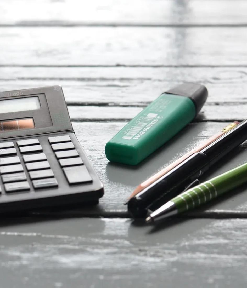Overhead view of a wooden desk with a solar calculator and a row of pens and markers laid out beside it