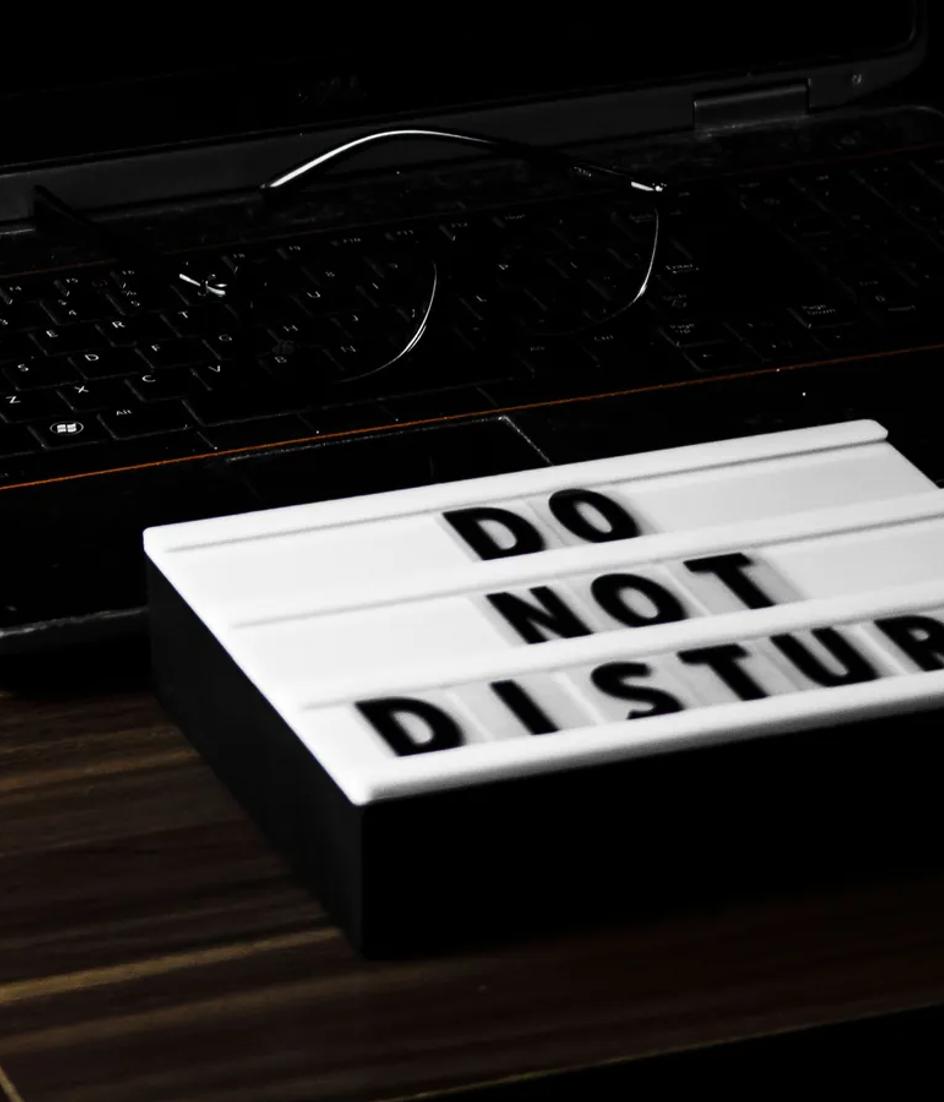 Un portátil sobre un escritorio en penumbra muestra la hora en pantalla, junto a un cartel de no molestar.
