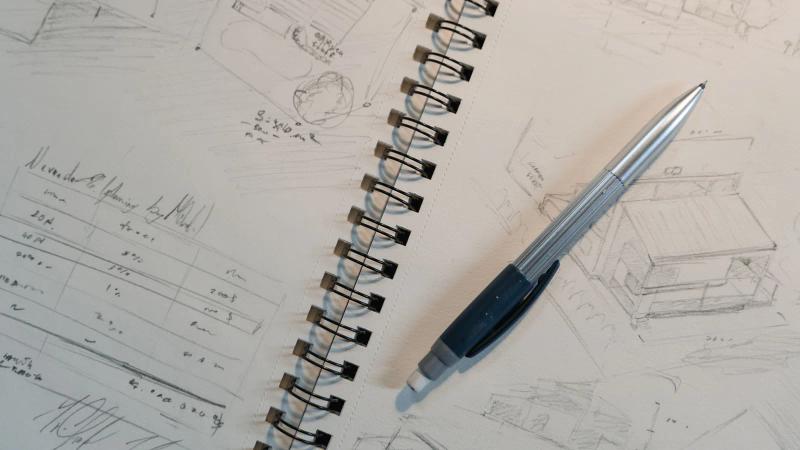 Un portaminas sobre un cuaderno de espiral lleno de bocetos pequeños dibujados a tamaño de miniatura.