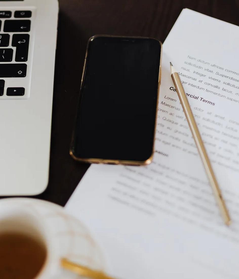 A printed contract lying open on a desk beside a laptop and a phone, the paper the compliance duty actually travels on
