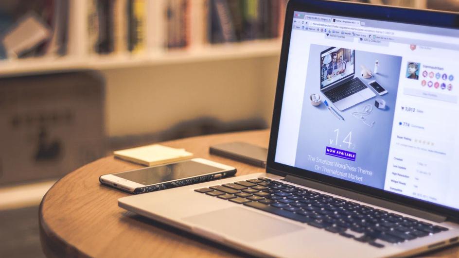 A laptop open on a wooden table next to a smartphone, the two screens a business site has to work on.