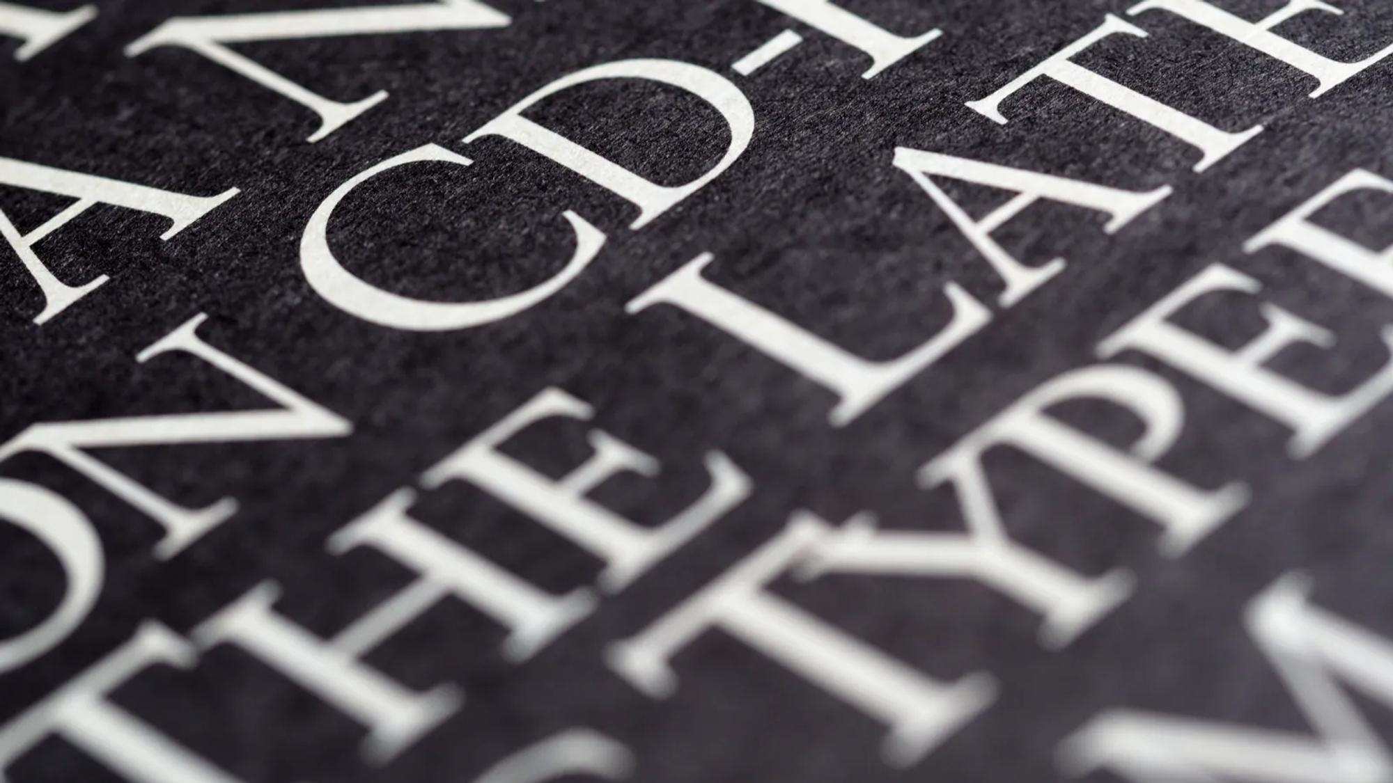 Letras blancas impresas sobre papel negro, en primer plano, donde se ve cómo aguantan los contraformas con contraste alto.