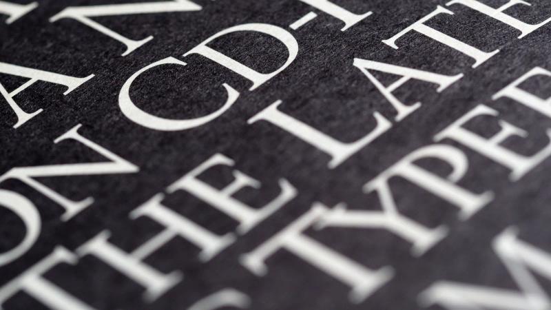 Letras blancas impresas sobre papel negro, en primer plano, donde se ve cómo aguantan los contraformas con contraste alto.
