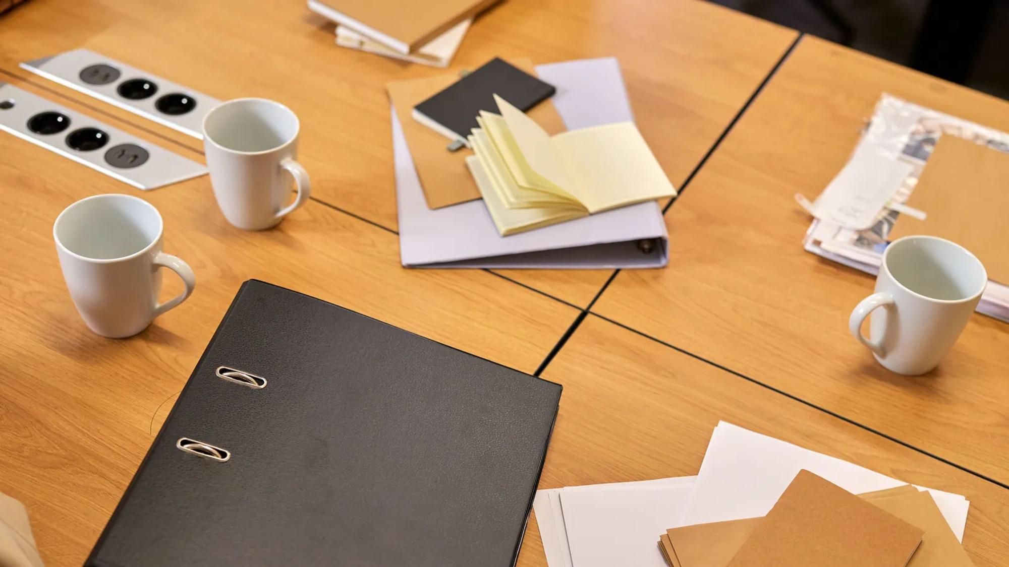 Binders and loose printed pages arranged on a wooden desk, the paperwork a fixed-scope quote turns into.
