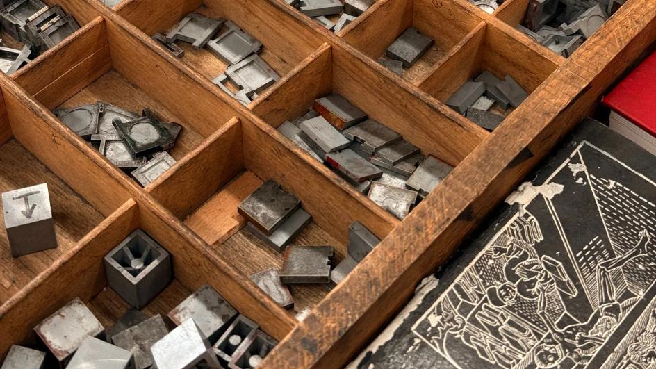 Metal letterpress blocks packed into a wooden tray, each glyph cut at the exact size it will print at.