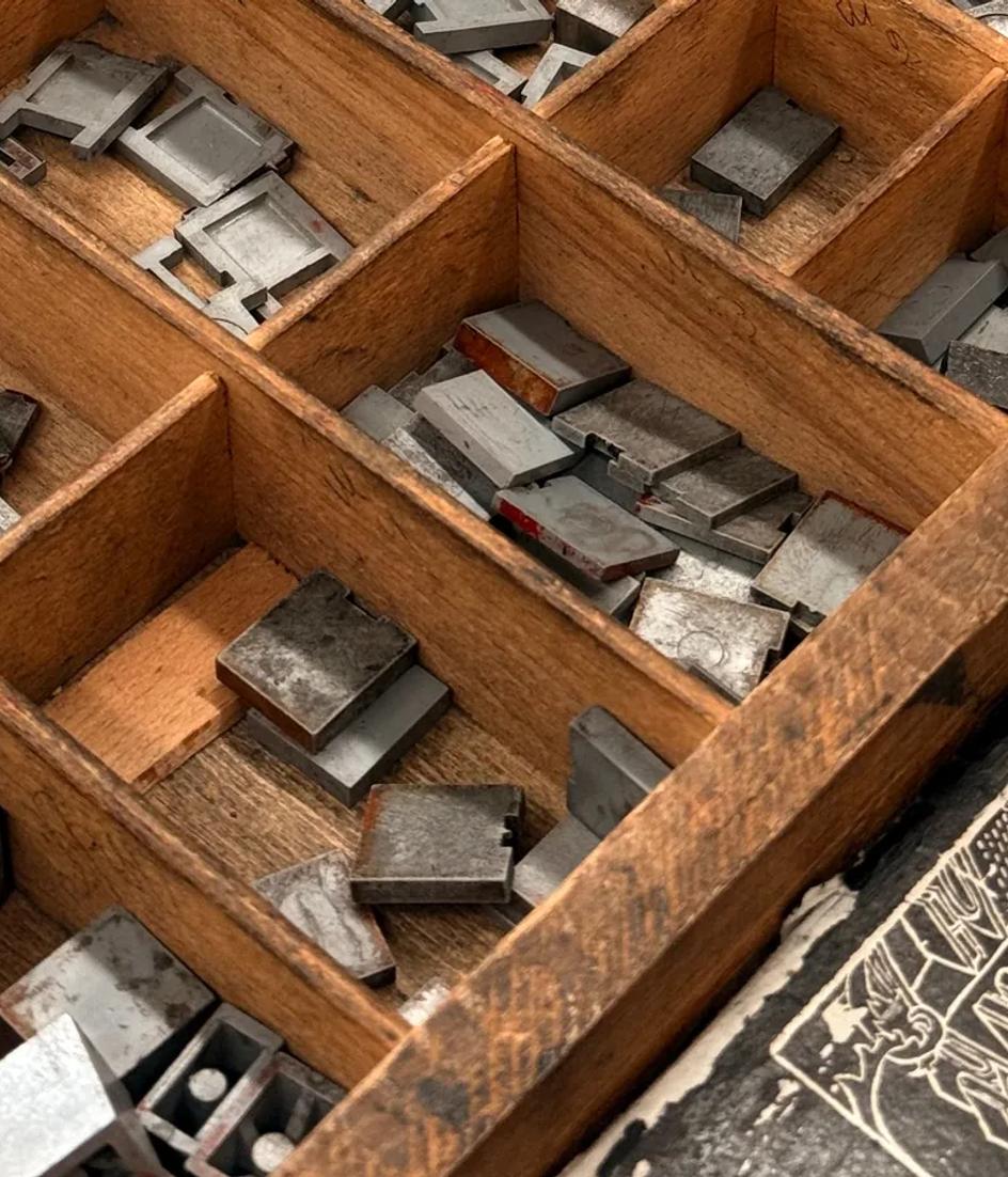 Metal letterpress blocks packed into a wooden tray, each glyph cut at the exact size it will print at.