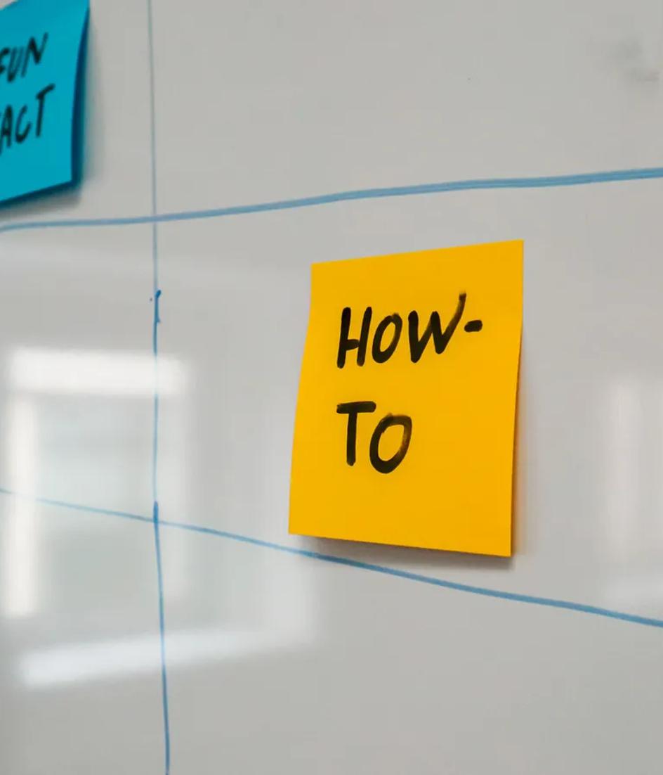 Coloured sticky notes taped across a whiteboard schedule, one team's work laid out as a single visible sequence of stages.